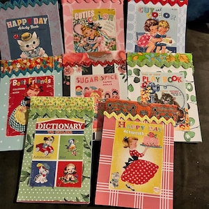 May include: A collection of vintage-style activity books with colorful covers. Titles include "Happy Day," "Cuties to Color," and "Best Friends." The books feature illustrations of children, animals, and various activities, with decorative trim.