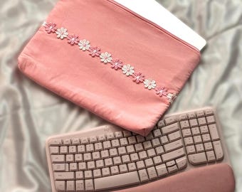 May include: A pink laptop sleeve with a white and pink floral design. A pink ergonomic keyboard with a wrist rest is also pictured.