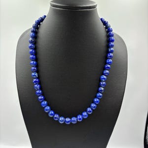 May include: A necklace of deep blue, round beads displayed on a black mannequin. The beads have a slightly irregular shape and a polished finish. The necklace is a classic jewelry piece, suitable for various occasions.