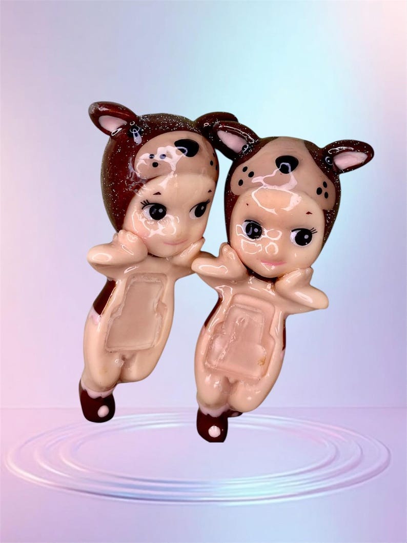 Pu&ograve; includere: Due figurine in ceramica di bambini vestiti con costumi da cucciolo marroni e bianchi. Le figurine sono in piedi su uno sfondo blu chiaro con un effetto increspato.
