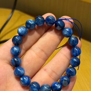 Puede incluir: Una pulsera con cuentas redondas y pulidas de color azul. Las cuentas están ensartadas en un cordón azul, creando un diseño circular. Las cuentas tienen un aspecto veteado, con tonos más claros y oscuros de azul.