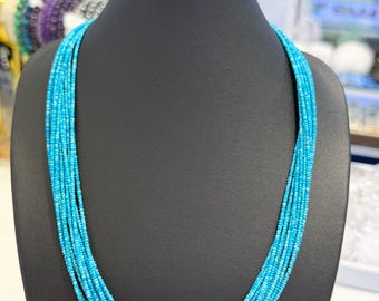 May include: A multi-strand necklace featuring numerous rows of small, bright turquoise blue beads. The necklace is displayed on a black neck form, showcasing the uniform size and vibrant color of the tiny, round beads that create a layered effect.