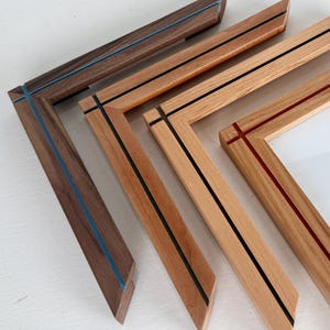 May include: Four wooden picture frames arranged in a cascading layout. The frames feature inlaid colored lines, including blue, black, and red accents. One frame contains a white insert with the text "SIGNED & NUMBERED" and a graphic illustration.