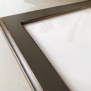 May include: A rectangular picture frame with a dark charcoal gray finish and visible copper-toned distressing along the inner and outer edges. The frame features a smooth, flat surface profile and surrounds a plain white rectangular center area.