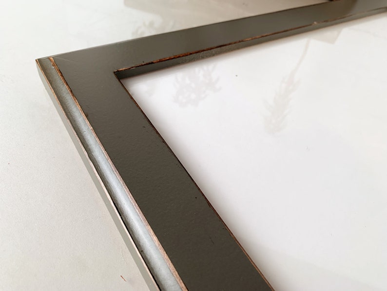 May include: A rectangular picture frame with a dark charcoal gray finish and visible copper-toned distressing along the inner and outer edges. The frame features a smooth, flat surface profile and surrounds a plain white rectangular center area.