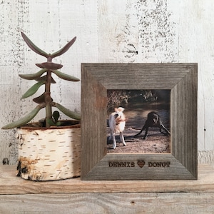 May include: A rustic wooden picture frame with a photo of two dogs playing in a field. The frame is engraved with the names "Dennis" and "Donut" and a heart symbol.