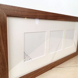 May include: A rectangular wooden picture frame with three openings. The frame is made of dark brown wood and has a white matting. The frame is designed to hold three photos or artworks.