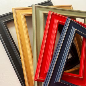 May include: A collection of colorful picture frames in various shades, including black, gold, green, red, and blue. The frames are arranged in a slightly overlapping fan shape, showcasing their different colors and textures.