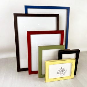 May include: A collection of rectangular picture frames in various colors, including brown, red, green, black, blue, and yellow. The frames are empty, with white interiors. The yellow frame has the text "SIGNED NUMBERED" and a logo.