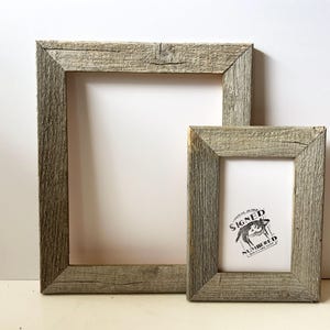 May include: Two rustic, rectangular wooden picture frames. The larger frame is empty, while the smaller frame contains a black and white graphic with text. Both frames have a weathered, gray finish.