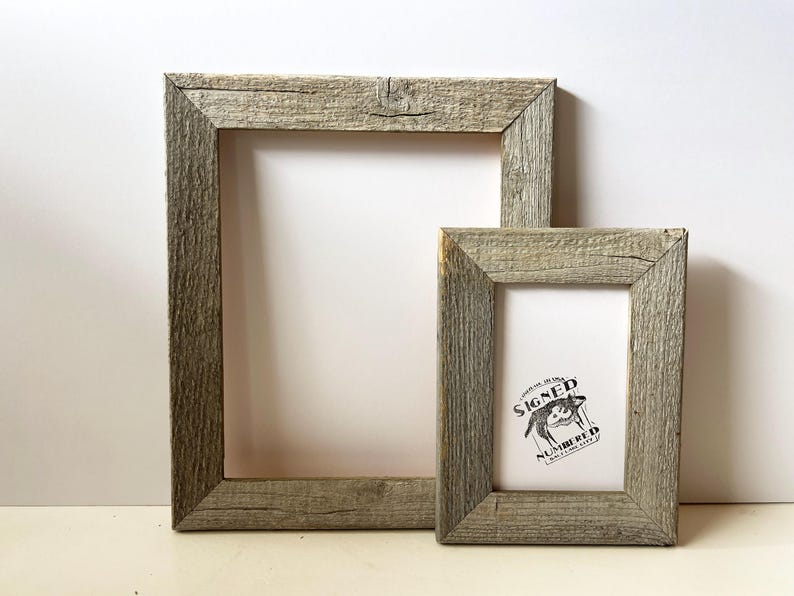 May include: Two rustic, rectangular wooden picture frames. The larger frame is empty, while the smaller frame contains a black and white graphic with text. Both frames have a weathered, gray finish.