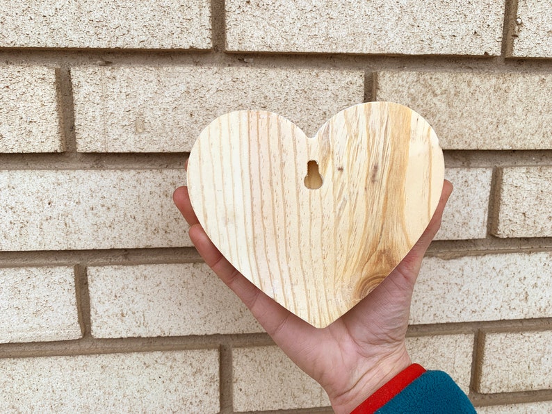 May include: A plain wooden heart-shaped ornament with a hole for hanging. The heart is light brown and has a natural wood grain.