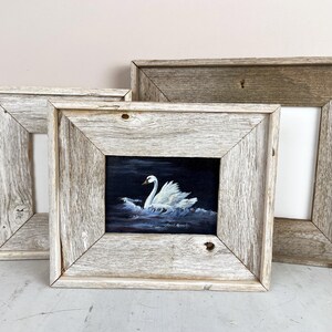 May include: Three rustic wooden picture frames. One frame contains a painting of a white swan on dark blue water. The frames are made of weathered, light gray wood. The frames are empty, ready for photos or art.