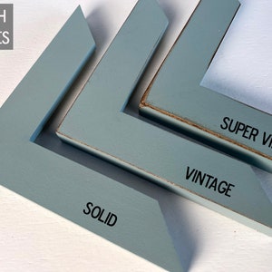 May include: Three L-shaped blue wooden frame corner samples labeled FINISH STYLES. The first is labeled SOLID with a smooth finish. The second is labeled VINTAGE with worn edges. The third is labeled SUPER VINTAGE with heavily distressed edges.