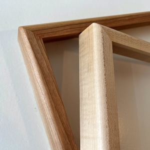 May include: Two wooden picture frames, one on top of the other. The top frame is a lighter wood color and the bottom frame is a darker wood color.
