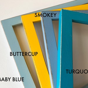 May include: Four wooden picture frames in different colors: baby blue, buttercup yellow, smokey blue, and turquoise. The frames are stacked on top of each other.