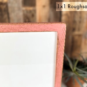 May include: A corner section of a rectangular frame with a rough-sawn texture and a dusty pink finish. The frame surrounds a plain white center panel. The text 1x1 Roughsawn is visible in the upper right corner of the image against a light background.
