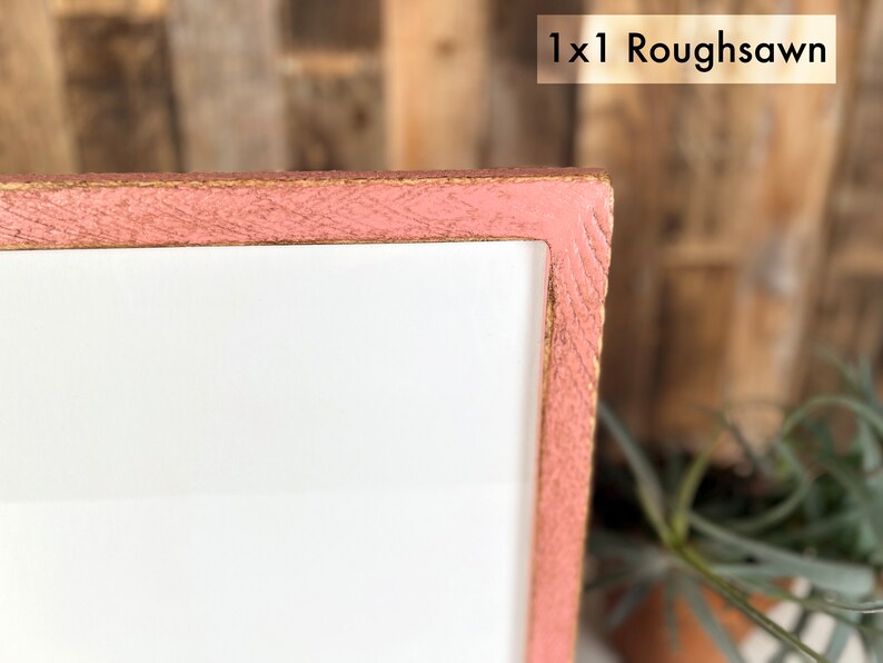 May include: A corner section of a rectangular frame with a rough-sawn texture and a dusty pink finish. The frame surrounds a plain white center panel. The text 1x1 Roughsawn is visible in the upper right corner of the image against a light background.