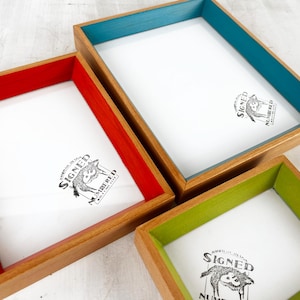 May include: Three wooden picture frames with colorful interior borders in red, teal, and green. The frames have a natural wood finish and contain a white insert with a black and white illustration and text.