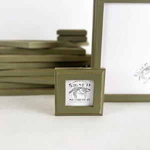 May include: A stack of green picture frames with a smaller green frame in the foreground. The smaller frame has a white mat and a black and white print that reads "Signed & Numbered".