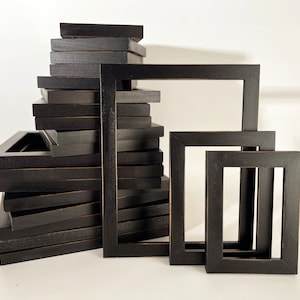 May include: A stack of black picture frames of various sizes. The frames are made of wood and have a simple, modern design.