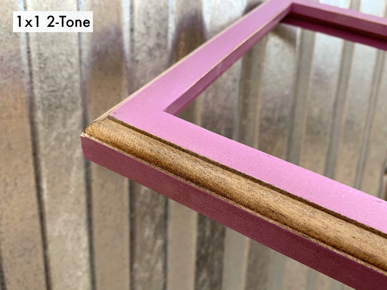May include: A rectangular picture frame featuring a two-tone finish with a matte pink outer edge and a natural wood-toned inner trim. The frame has a beveled profile and includes the text 1x1 2-Tone in the upper left corner of the image.