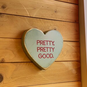 May include: A light blue wooden heart-shaped sign with the text "PRETTY, PRETTY GOOD." in red lettering.