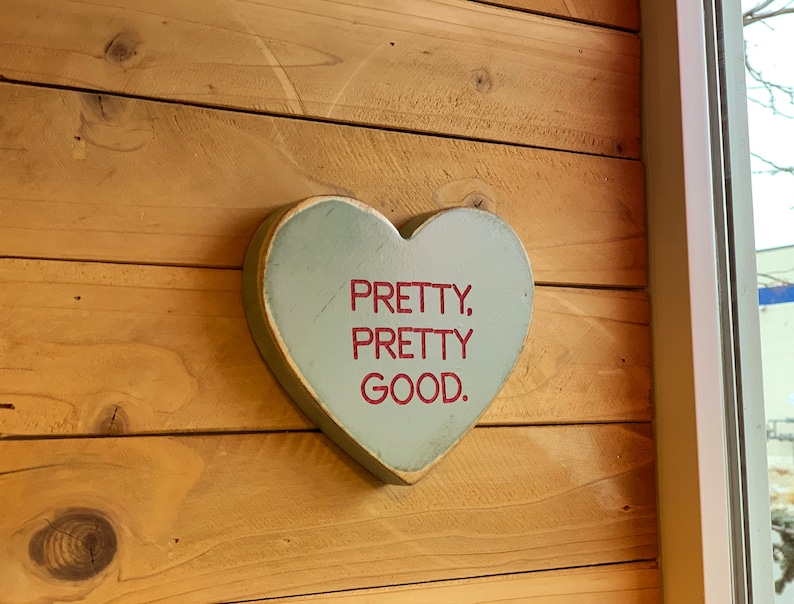 May include: A light blue wooden heart-shaped sign with the text "PRETTY, PRETTY GOOD." in red lettering.