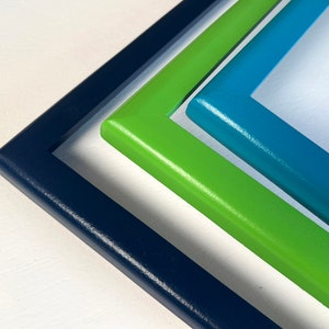 May include: Three picture frames, nested inside each other, with a navy blue frame on the bottom, a green frame in the middle, and a teal blue frame on top.