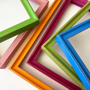 May include: A set of five colorful picture frames, each with a different color and a gold trim. The frames are stacked on top of each other, with the green frame on top and the blue frame on the bottom.