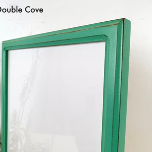 May include: A rectangular picture frame with a mint green finish and distressed dark brown edges. The frame features a double cove profile and includes the text 1x1 Double Cove in the upper left corner, surrounding a blank white center.
