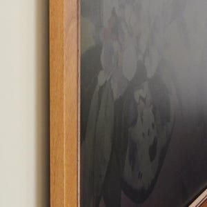 Peut inclure: Une &oelig;uvre d'art encadr&eacute;e repr&eacute;sentant une nature morte florale aux tons sourds. Le cadre en bois est de couleur marron clair et chaleureux. L'&oelig;uvre est accroch&eacute;e au mur.