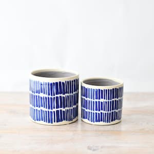 May include: Two cylindrical ceramic planters featuring a hand-painted pattern of vertical dark blue dashes arranged in horizontal rows against a cream-coloured background. The interior of each vessel is finished in a smooth, solid light grey glaze.