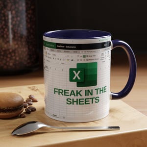 May include: A white ceramic mug with a blue rim and handle. The mug features a green and white Microsoft Excel spreadsheet with the text "FREAK IN THE SHEETS" printed below.