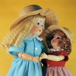 May include: Two porcelain dolls wearing straw hats and dresses. The doll on the left is wearing a blue and white gingham dress and a light blue shirt. The doll on the right is wearing a red and white gingham dress and a white shirt.