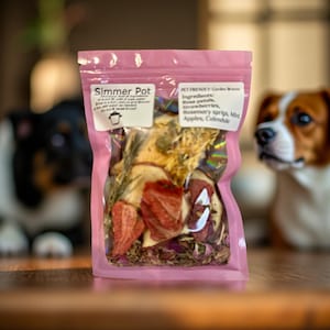 May include: A pink, resealable bag labeled "Simmer Pot" filled with dried ingredients. The ingredients include rose petals, strawberries, rosemary sprigs, mint, apples, and calendula. The bag is in front of a blurred background with two dog figurines.