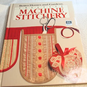 May include: A book titled "Better Homes and Gardens Creative Machine Stitchery" with a red and tan design. The cover features a sewing project with scissors, a heart-shaped decoration, and a pocket design.