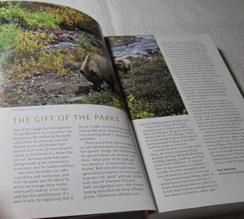 May include: A book open to a photograph of a bear in a natural environment. The text "THE GIFT OF THE PARKS" is displayed, accompanied by text discussing national parks and conservation.