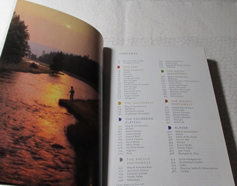 May include: Open book with a photograph of a person fishing in a river at sunset. The right page shows a detailed table of contents with various geographical regions.