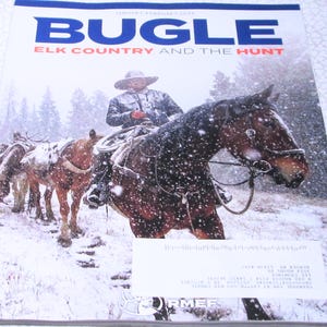 May include: The cover of a magazine titled "BUGLE" with the subtitle "ELK COUNTRY AND THE HUNT." The image depicts a cowboy on horseback leading a pack of horses through a snowy landscape. The magazine's masthead is blue and white.