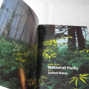 May include: Open book with a forest scene and yellow flowers. The cover reads "Guide to the National Parks of the United States."