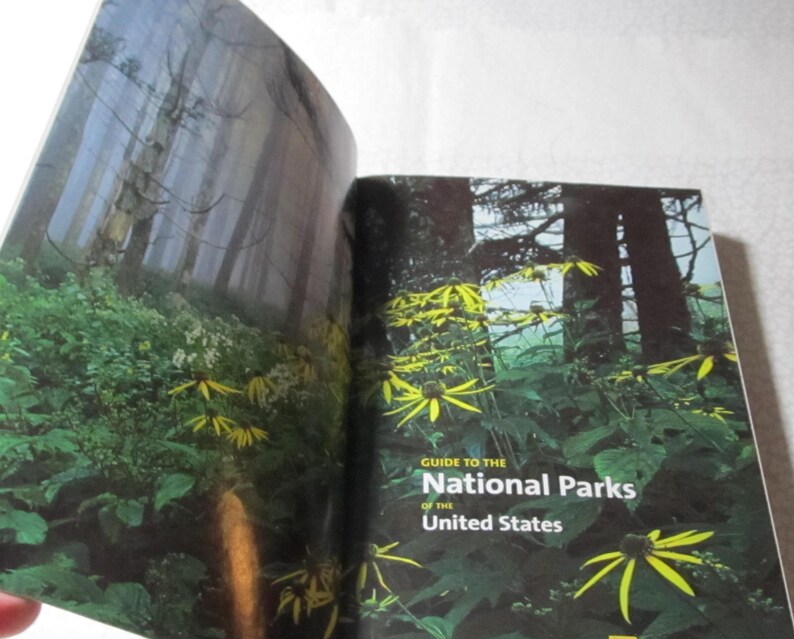 May include: Open book with a forest scene and yellow flowers. The cover reads "Guide to the National Parks of the United States."