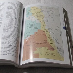 May include: An open book displaying a detailed map of a national park, with areas labelled "Capitol Reef," "Dixie National Forest," and "Grand Staircase-Escalante National Monument." The map is colourful, with shades of green, yellow, and brown.