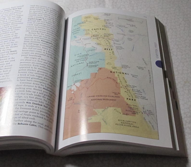 May include: An open book displaying a detailed map of a national park, with areas labelled "Capitol Reef," "Dixie National Forest," and "Grand Staircase-Escalante National Monument." The map is colourful, with shades of green, yellow, and brown.