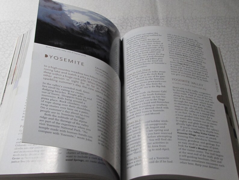 May include: An open book with a page featuring the word "YOSEMITE" and text describing Yosemite Valley. The page also includes a landscape photo of mountains. The book is open on a white surface.