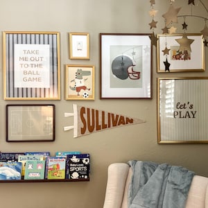 Peut inclure: Un mur de galerie avec des &oelig;uvres d'art encadr&eacute;es sur le th&egrave;me du sport. Comprend une banni&egrave;re "SULLIVAN" et une impression encadr&eacute;e avec "Take me out to the ball game". Un mobile en forme d'&eacute;toile est suspendu au plafond. Une &eacute;tag&egrave;re contient des livres pour enfants.