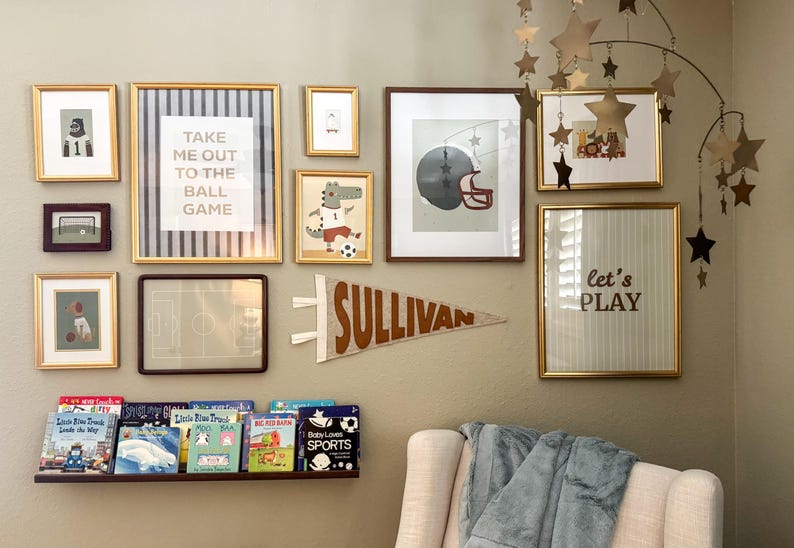 Peut inclure: Un mur de galerie avec des &oelig;uvres d'art encadr&eacute;es sur le th&egrave;me du sport. Comprend une banni&egrave;re "SULLIVAN" et une impression encadr&eacute;e avec "Take me out to the ball game". Un mobile en forme d'&eacute;toile est suspendu au plafond. Une &eacute;tag&egrave;re contient des livres pour enfants.