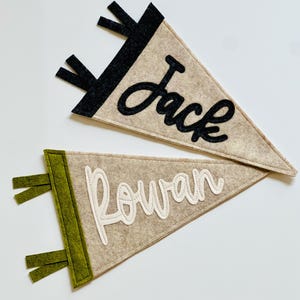 May include: Two felt pennants, one tan with black accents and the name "Jack" in black script, the other tan with green accents and the name "Rowan" in white script. Both have a triangular shape.