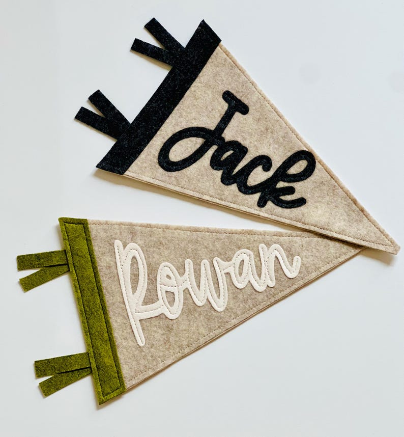 May include: Two felt pennants, one tan with black accents and the name "Jack" in black script, the other tan with green accents and the name "Rowan" in white script. Both have a triangular shape.