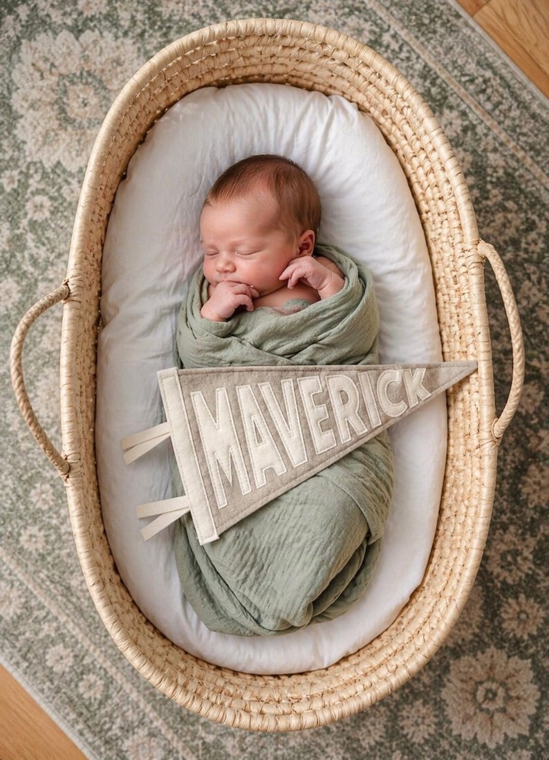Peut inclure: Un nouveau-n&eacute; endormi, envelopp&eacute; dans une couverture vert sauge, repose dans un panier en osier. Une banni&egrave;re avec le nom "MAVERICK" est plac&eacute;e pr&egrave;s du b&eacute;b&eacute;. Le panier est garni d'un drap blanc.
